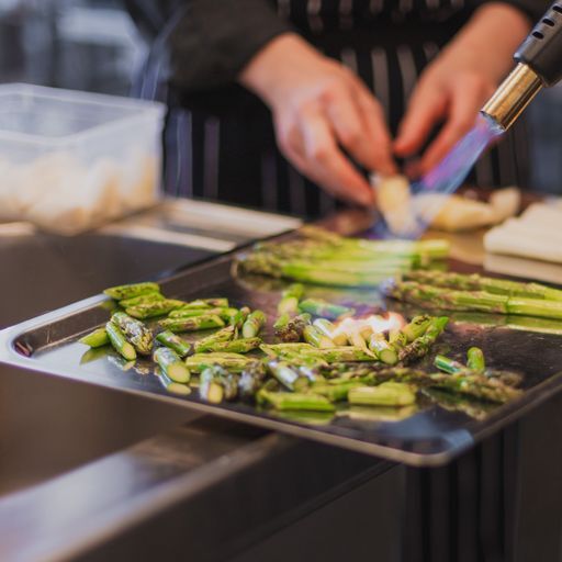 Kock som flamberar grillad sparris i köket